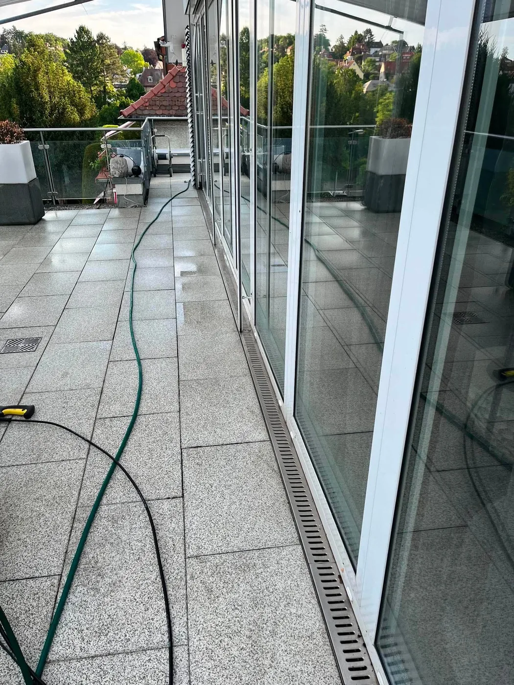 Terrassenplatten entlang einer Glasfront werden mit dem Hochdruckschlauch gereinigt – echtes Einsatzfoto